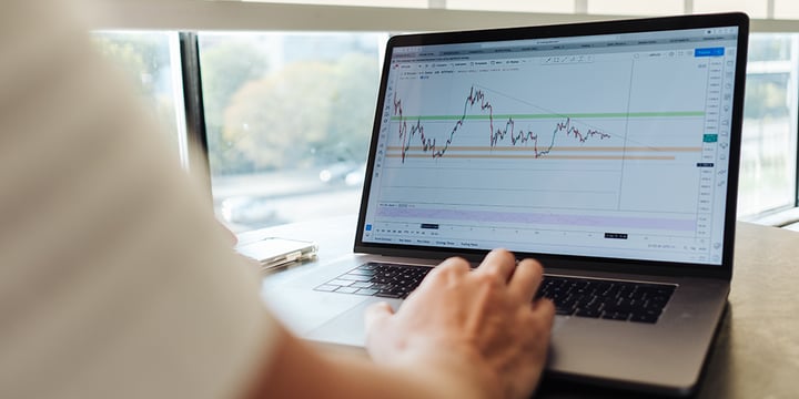 A hand is using a laptop. There is a graph displayed on the screen.