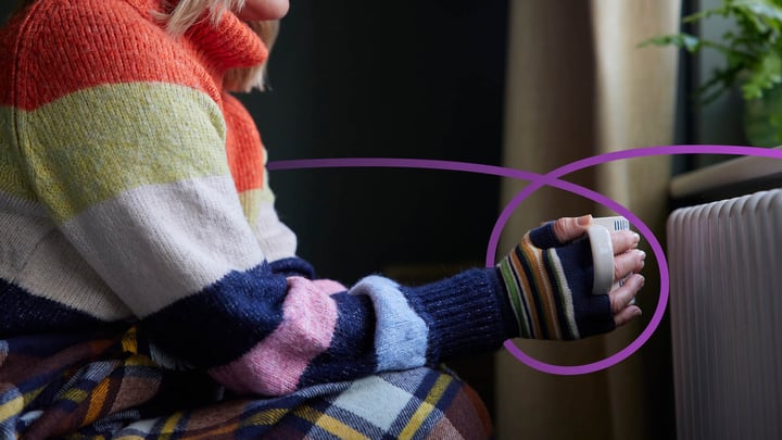 Lady wearing a jumper, gloves, and blanket whilst holding a cup of tea