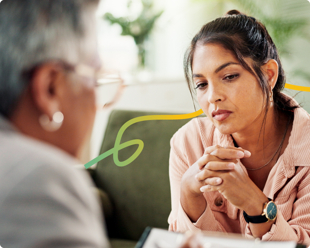 An over the shoulder shot of a therapist talking to their patient. The patient is a woman who has a sad expression on her face.