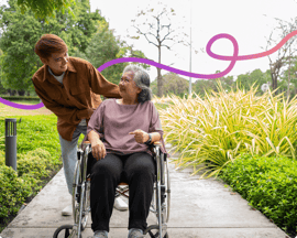 Image of a younger man pushing an older woman in a wheelchair and smiling