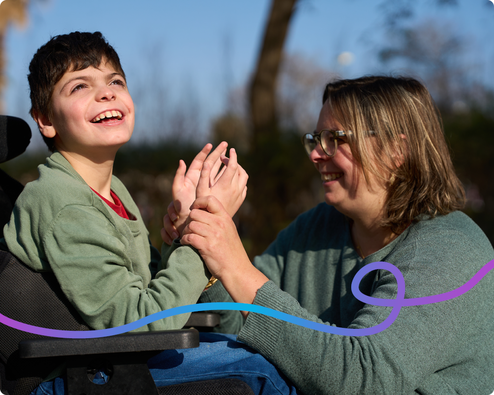 Image of a young boy in a wheelchair clapping his hands with his mum