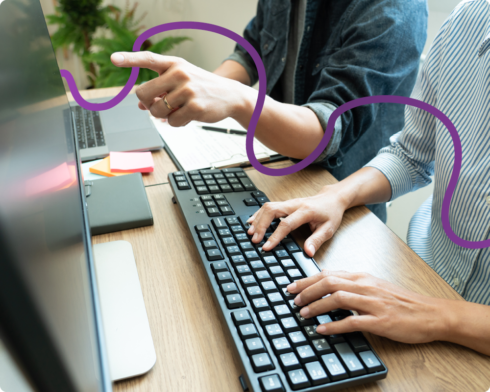 Image of hands where someone is typing on a computer and the other is pointing at the screen.