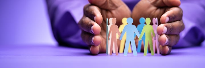 Hands protecting paper cut outs of people