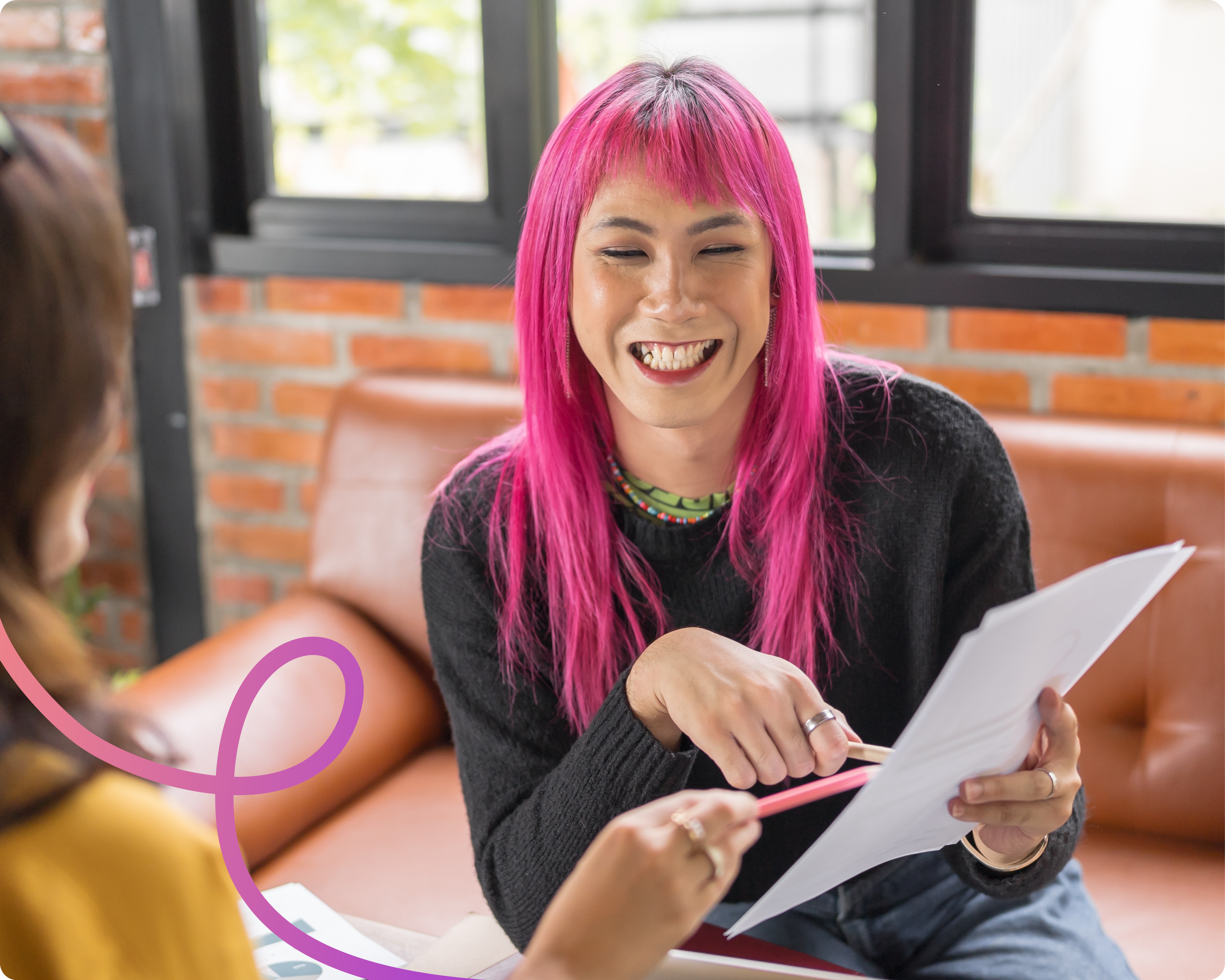 A woman with pink hair smiling whilst pointing to some documents