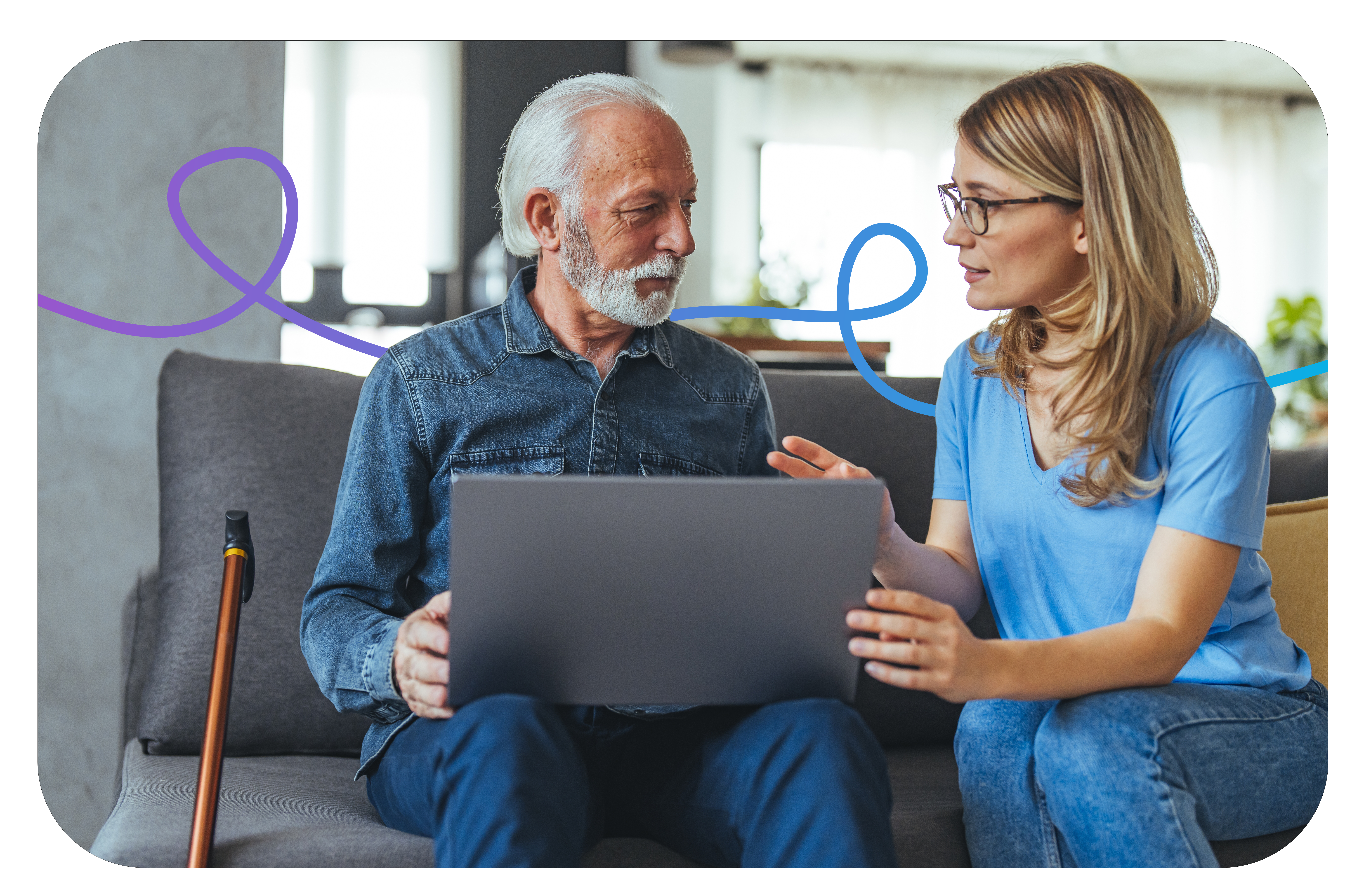 an elderly man sat on the sofa holding a laptop talking to a female trainer