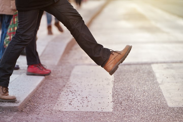 Man taking a step on to a zebra crossing. Only his legs are visible. 