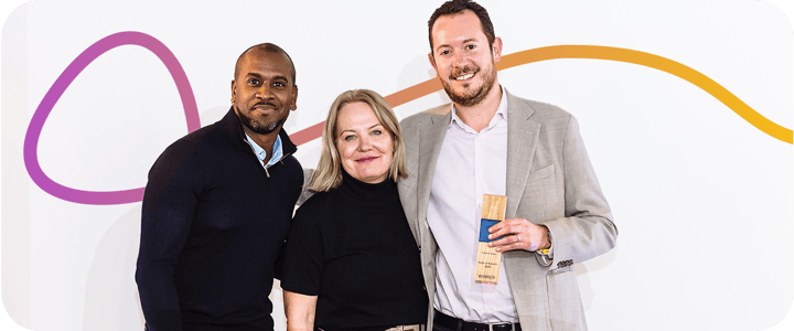 Matt Adam standing next to 2 hosts of the Impact Awards, holding his Founders Award trophy.