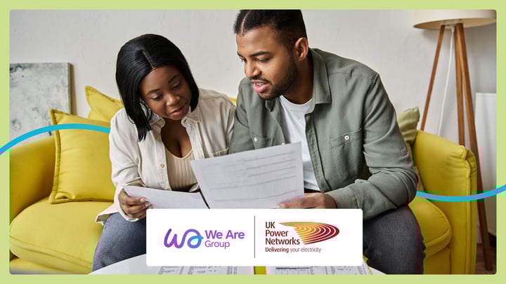 A young couple sitting on a sofa looking at their utility bills. The image is overlayed by We Are Group and UK Power Network's logos.
