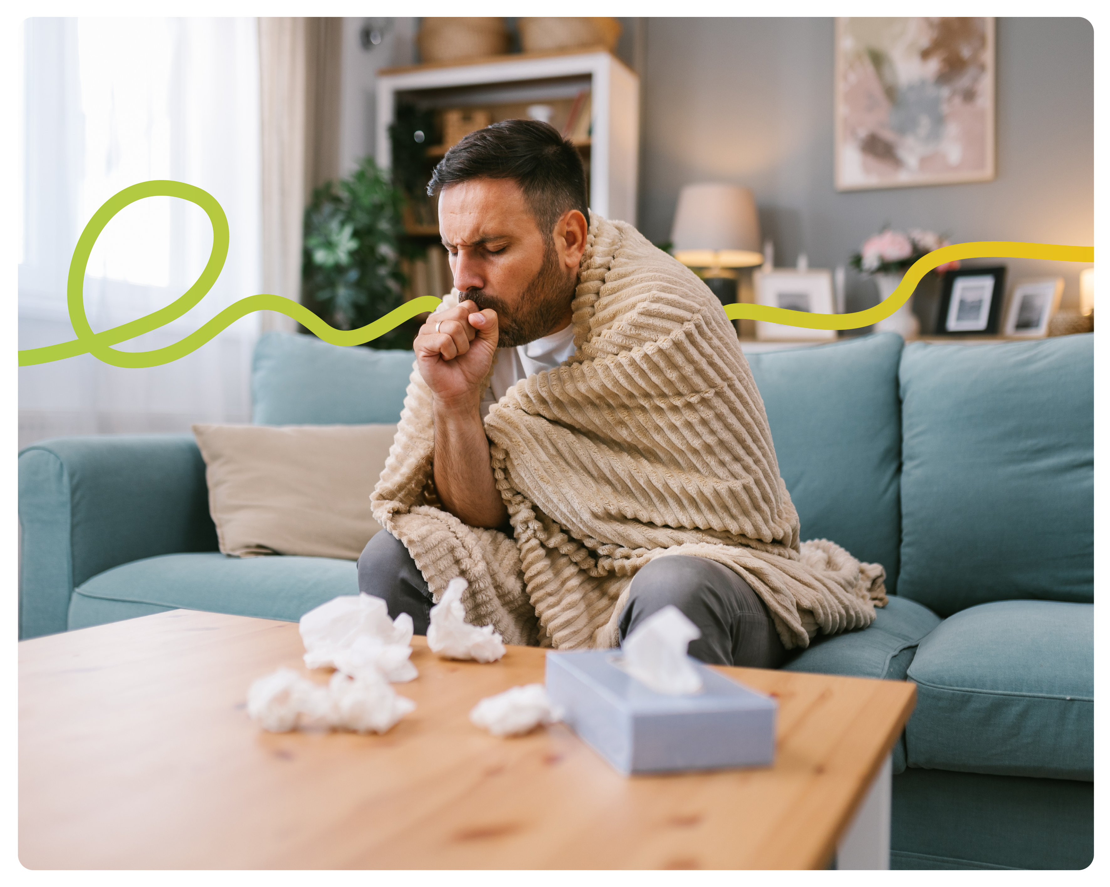 a man sat on his sofa, wrapped up in a blanket, coughing