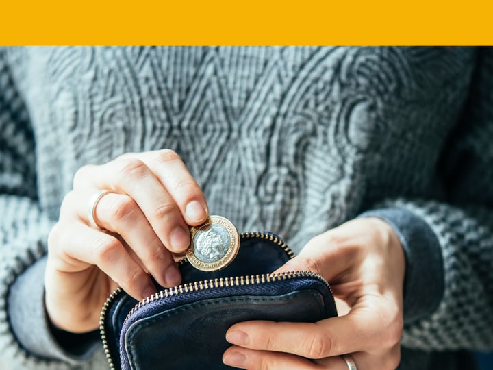 Hands are holding a wallet and putting a 1 pound coin inside the wallet. 