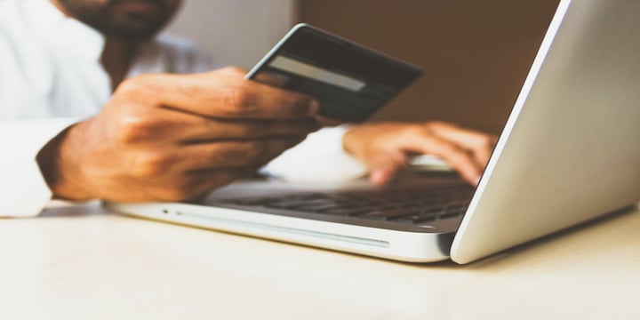 A man on a laptop using his bank card. His hands and bank card are shown in the image and a small proportion of the laptop.