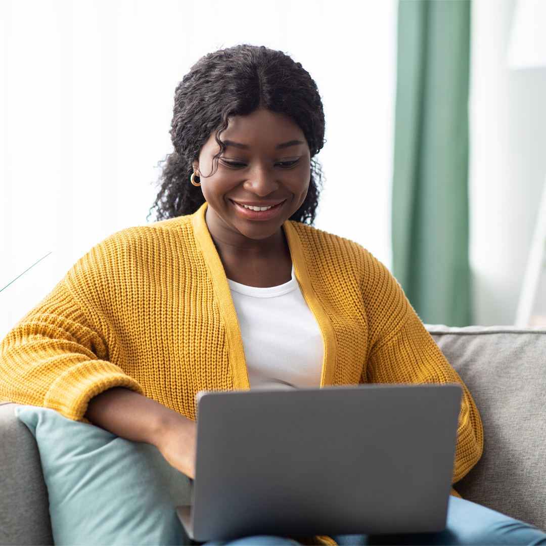 young woman smiling whilst using her laptop 1080 x 1080 px