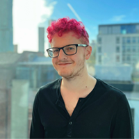 A person with bright pink hair smiling, with a city view in the background.