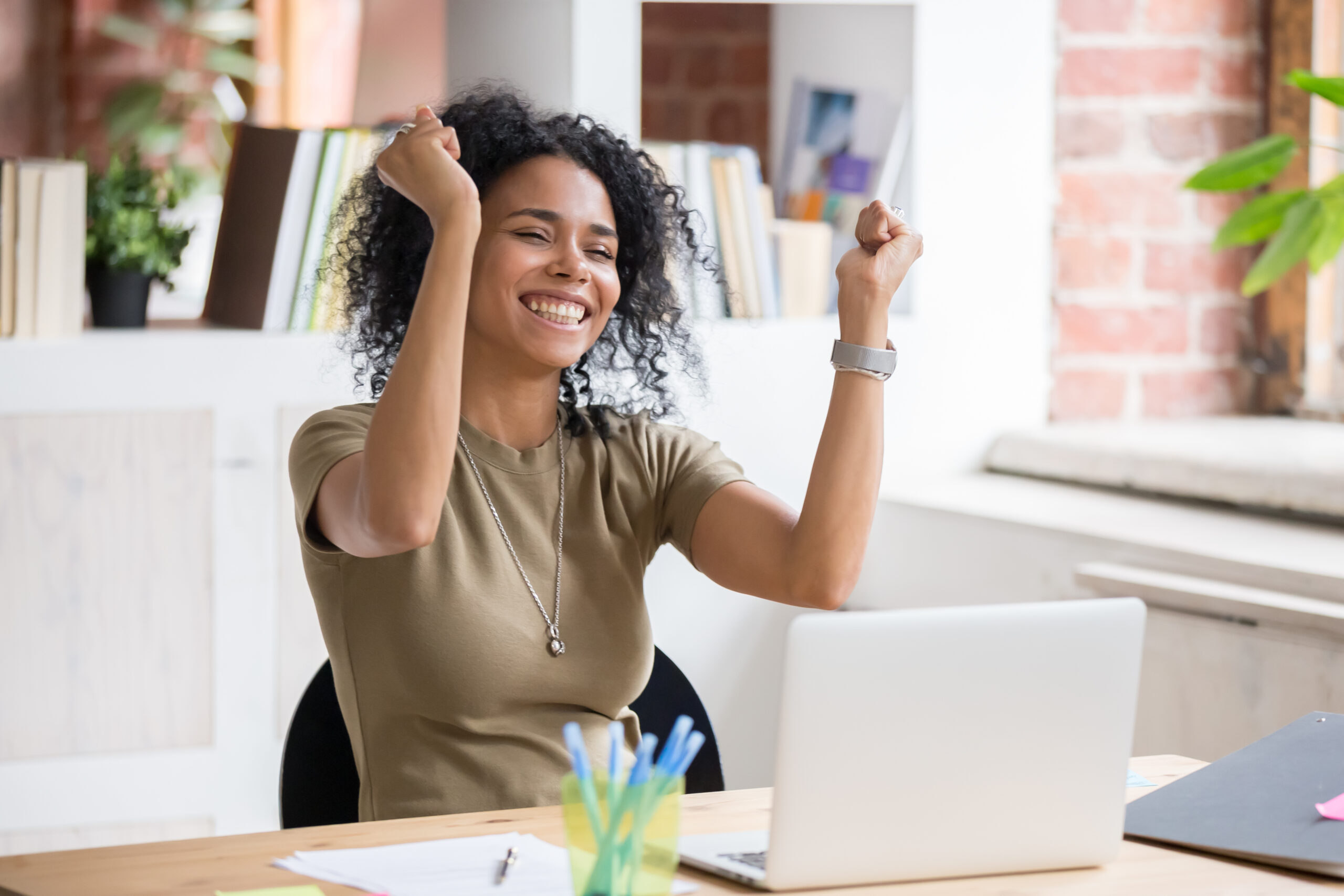 Woman sat at desk cheering at laptop screen