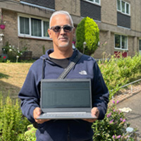 Image of an older man (Mohammed) smiling and holding a laptop provided by We Are Group