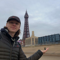 Image of a young man posing holding his hand out with hi friend in the background.